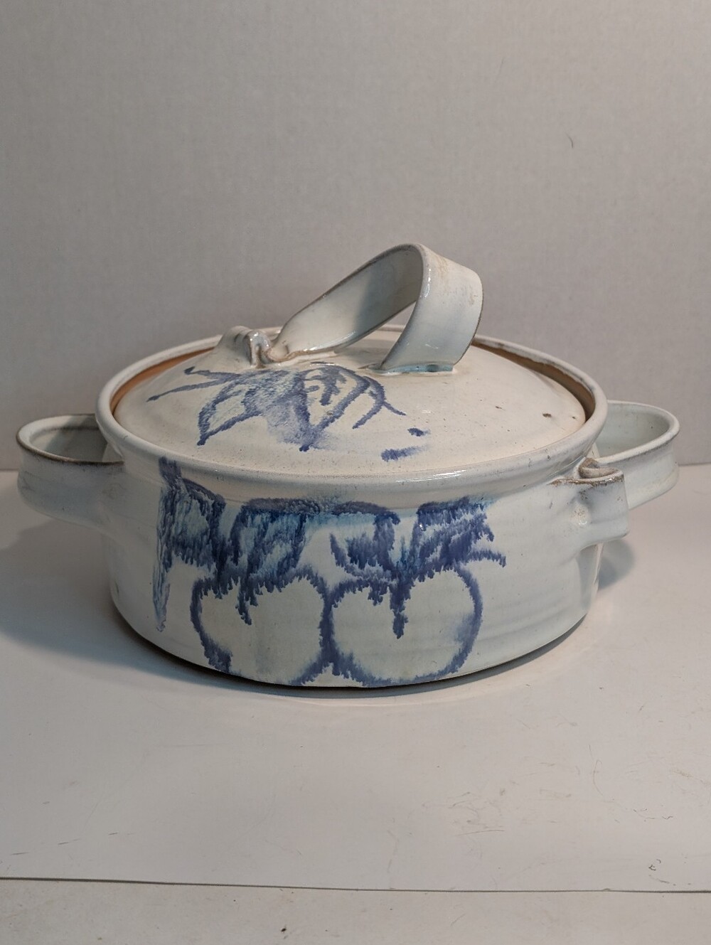 White ceramic casserole dish features a blue hand-painted floral design. Signed.